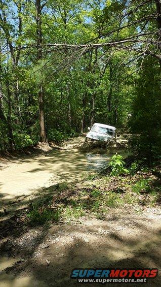 White SUV stuck deep in a muddy trail, surrounded by trees
