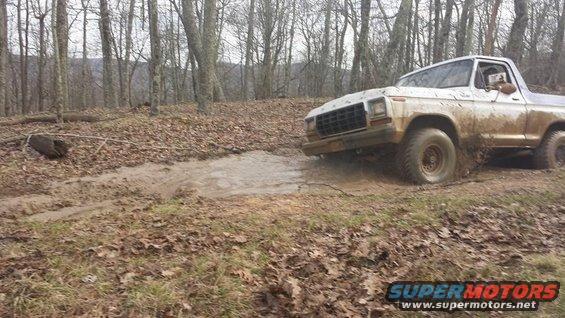 White 1979 Ford Bronco driving through mud in a wooded area