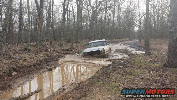 1979 Ford Bronco driving through a muddy trail in a forest