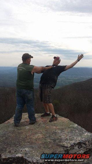 Two guys goofing around on a cliff edge with a scenic view