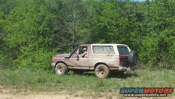 Muddy 1987 Ford Bronco with snorkel and spare tire on rear, parked on grassy trail