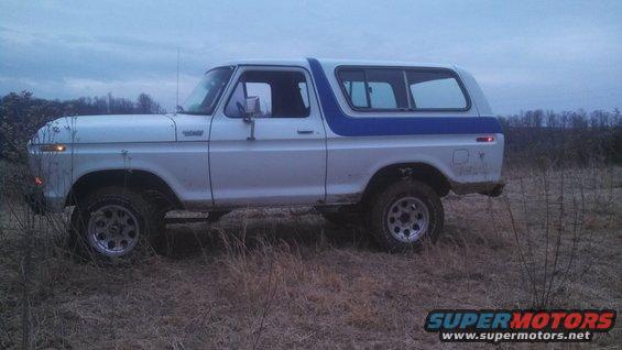 Side view of a 1979 Ford Bronco with a blue stripe, off-roading in a field