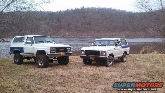 1978 Ford Bronco and a GMC Jimmy parked on dry grass near a lake