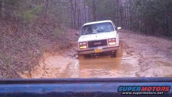 White GMC pickup truck with yellow license plate driving through a muddy trail
