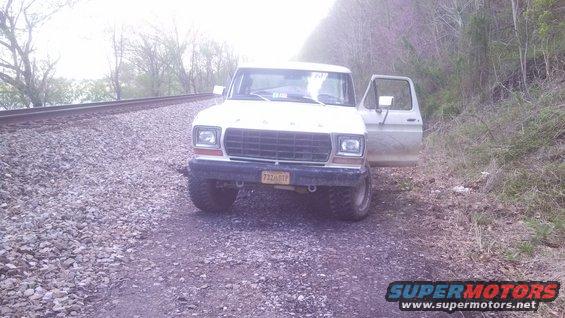 White 1979 Ford Bronco with open driver's door parked on a gravel road next to railroad tracks