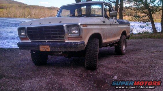 Ford Bronco parked by a body of water, trees in background