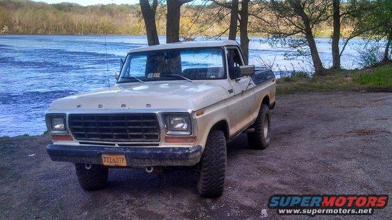 Tan 1977 Ford F-150 pickup truck with a blue bed cover parked on gravel near a river