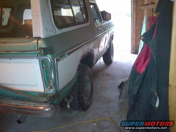Side view of a green and white 1978 Ford Bronco parked in a garage. A jacket hangs on the wall