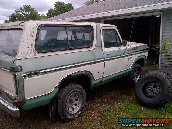 1978 Ford Bronco, two-tone green and white, showing rust and wear, parked next to a garage