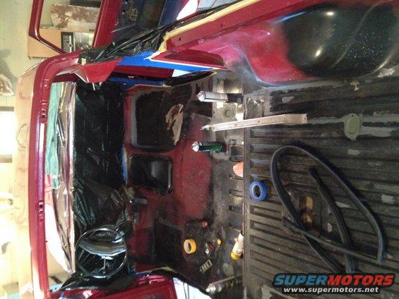 Interior of a red vehicle undergoing restoration, with black plastic sheeting covering parts of the cabin