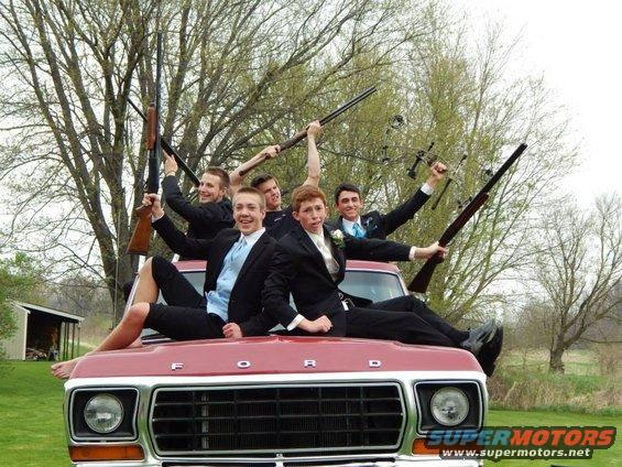 Red Ford truck front grille with five young men in suits sitting on hood holding rifles