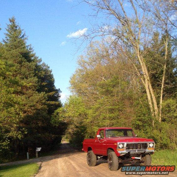 red 1978 Ford F-150 pickup truck on a dirt road, lifted with large tires