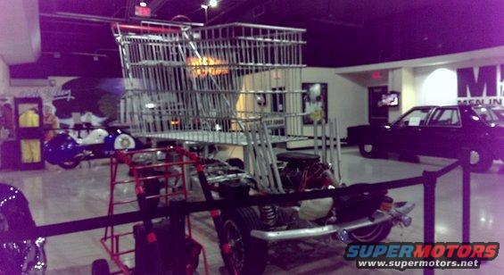 Custom vehicle with a giant shopping cart body on a chassis, viewed from the rear