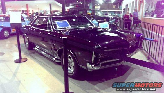Black 1966 Pontiac GTO with hood scoop and side pipes, parked indoors with other vehicles