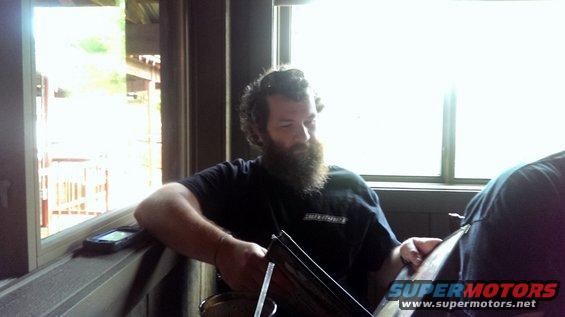 Man with beard sitting indoors with a phone on the windowsill