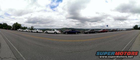 Line of 2000 Mercury Grand Marquis sedans parked on a scenic overlook, cloudy sky