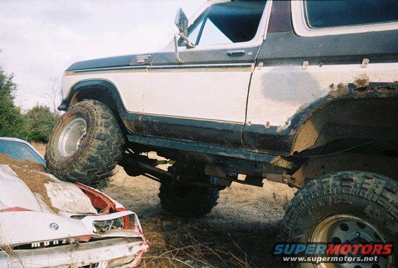 1978 Ford Bronco with large tires on top of a crushed car