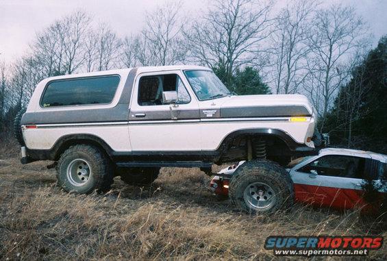 White and grey 1978 Ford Bronco lifted over a red and white car