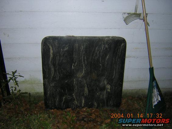 large tire with marbled pattern leaning against a white wall, rake and dustpan nearby