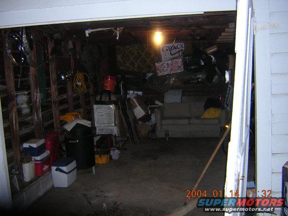 Cluttered garage interior with stacked coolers, trash cans, and a sofa