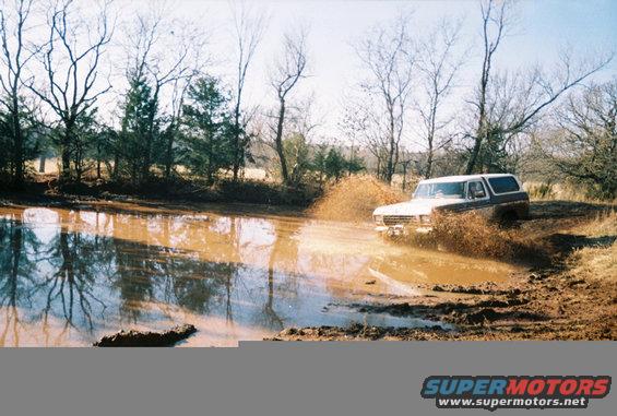 White and brown 1978 Ford Bronco driving through mud splash