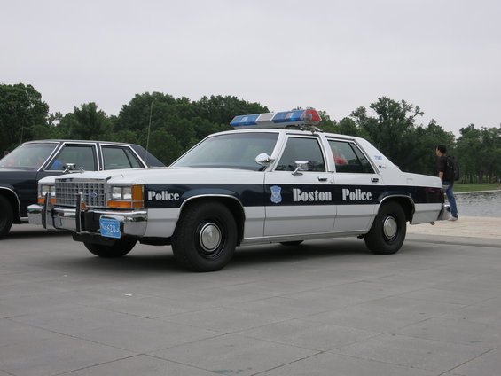 White and blue police car with light bar, parked next to another vehicle