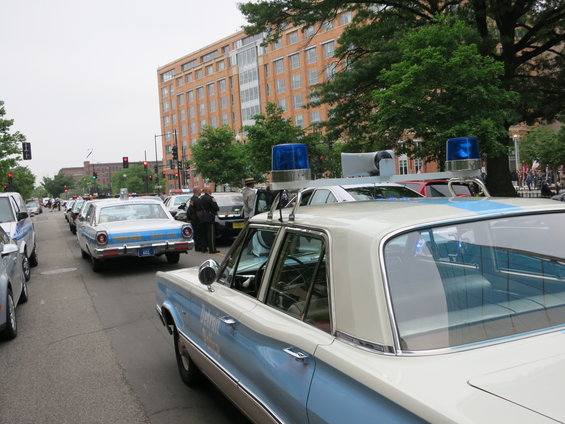 White and blue police car with blue lights, rear view. Text 'Detroit' visible on door