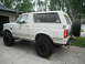 1990 Ford Bronco - This white SUV features oversized tires and a rear-mounted spare, suggesting off-road modifications.