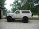 1990 Ford Bronco - White 1990 Ford Bronco lifted with large off-road tires sits on a concrete driveway.