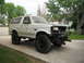 1990 Ford Bronco - This modified Ford Bronco sits on a driveway with a house and trees in the background.