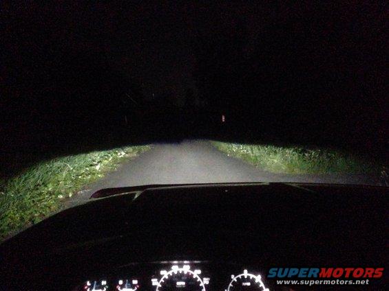 view from inside car at night, headlights illuminate road ahead, dashboard gauges visible