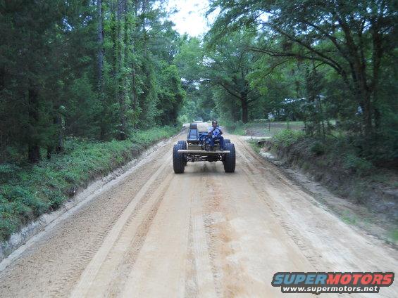 Custom buggy with exposed frame, two seats, and large tires drives on a dirt road