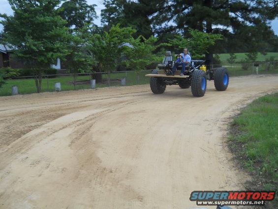 Custom off-road vehicle with large tires and wooden platform driving on dirt road