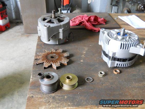 Two alternators, a rusty fan, two pulleys, and nuts on a workbench