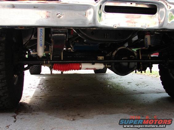 Undercarriage of a truck showing front axle, steering linkage with red boot, and Heckethorn shocks