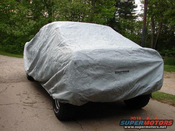 Car covered by a grey tarp, showing tires and a Rustoleum logo