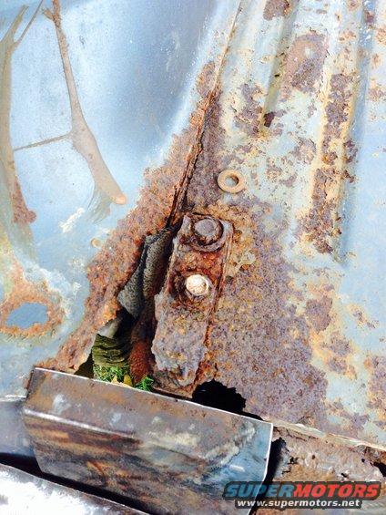 Close-up of heavily rusted metal panel with bolts and a washer. Some light blue paint is visible