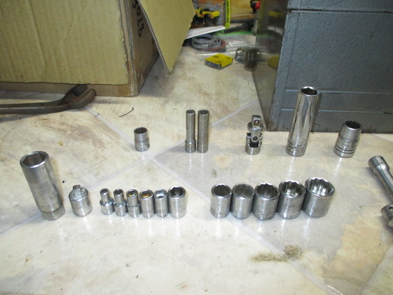 Socket set and a large wrench on a tiled floor, with a cardboard box and tool chest in the background