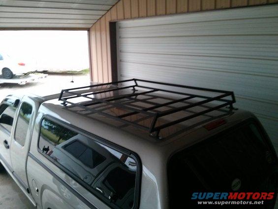 Silver pickup truck with a camper shell and a black roof rack, parked in a garage