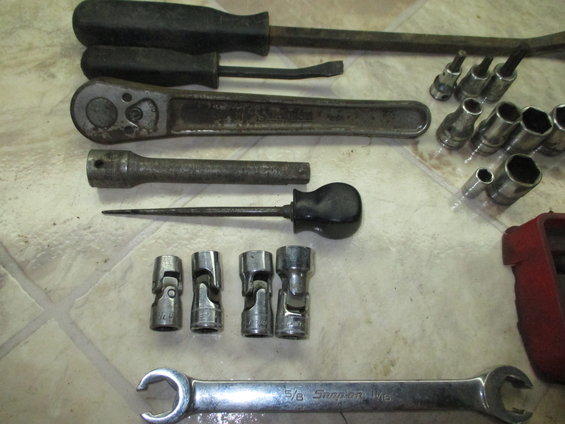 Socket wrench set, screwdrivers, and a pry bar on a tiled surface