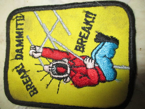 Yellow embroidered patch with black border showing a cartoon figure in red shirt and blue pants hanging from wires, with text "DAMMIT!" and "BREAK!!"