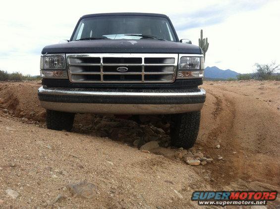 Front view of a 1994 Ford Bronco driving on a dirt road in a desert landscape
