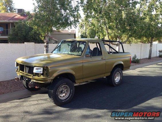 Olive green Ford Bronco with roll cage, parked on street