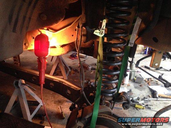 Suspension repair with coil spring held by straps, red work light illuminates frame
