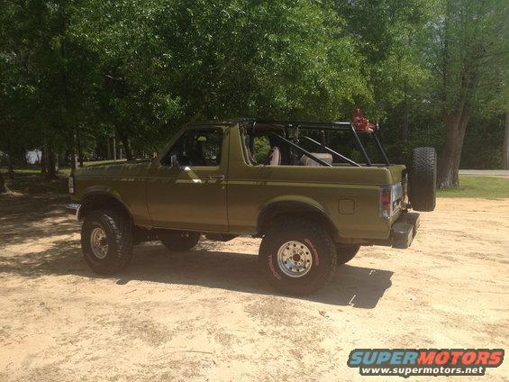 Olive green Ford Bronco with roll cage and spare tire on rear, lifted suspension