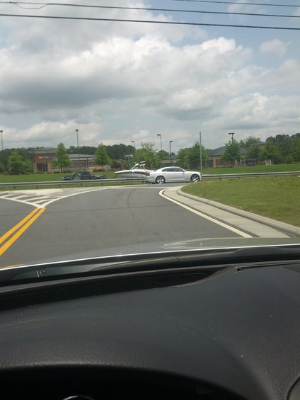 White sedan towing a boat on a road with a building in the background