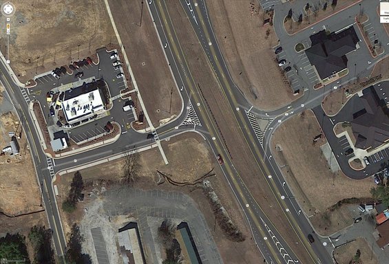 Red sedan driving on a highway next to a McDonald's