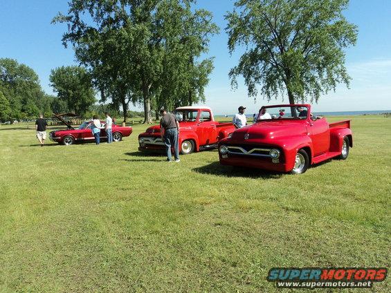 Three red classic vehicles parked on grass, two pickup trucks and one convertible