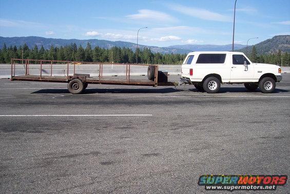 White 1990 Ford Bronco towing a flatbed trailer on a highway