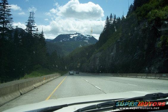driving on a highway through a mountainous area with trees and clouds